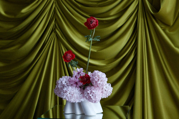 Floral arrangement in ceramic vase on a table with green draped fabric in the background
